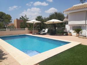 a swimming pool with umbrellas next to a house at Chalet con dos apartamentos in La Azohía