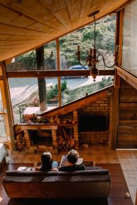 two people sitting on a couch in a room with a large window at Reserva Três Picos Chalés in Nova Friburgo