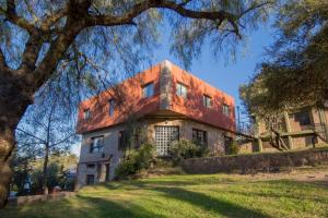 ein altes Haus mit rotem Dach auf einem Grasfeld in der Unterkunft Hotel La Colina del Sol in Villa Carlos Paz