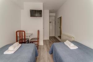 two beds in a room with a table and chairs at Hostal Lar in Burgos