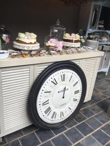 une grande horloge assise au-dessus d'une table avec des gâteaux dans l'établissement Villa Brocant Guest house, à Vryburg