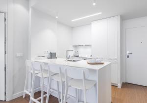 a white kitchen with a white counter and stools at Francisco Silvela Apartment by Flatsweethome in Madrid