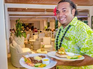 a man holding two plates of food in a restaurant at Muri Beach Club Hotel in Rarotonga