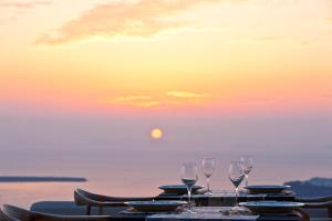 - une table avec des verres à vin et le coucher du soleil dans l'établissement Gold Suites - Small Luxury Hotels of the World, à Imerovigli