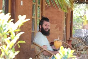 een man met een baard aan een tafel met een drankje bij Wild Breeze in Tissamaharama