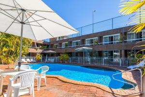 
a patio area with a pool, chairs, and an umbrella at Aquajet Motel in Coffs Harbour
