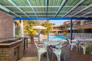 un patio con tavoli, sedie e piscina di Aquajet Motel a Coffs Harbour