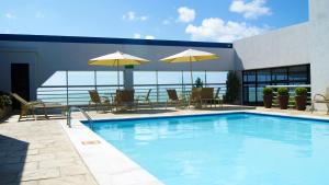 a swimming pool with tables and chairs and umbrellas at Littoral Tambaú Flat in João Pessoa