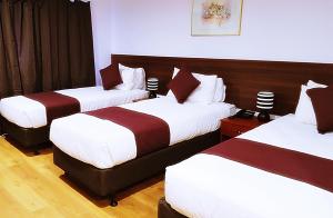 a hotel room with three beds with white and red sheets at Airport Garden Inn Hotel & Conference Centre in Auckland