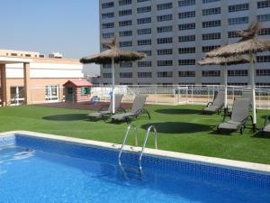 a swimming pool with chairs and umbrellas next to a building at Aparthotel Albufera in Alfafar