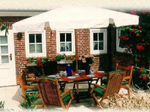 a table with chairs and a white umbrella in front of a house at Landjägerhaus am Südstrand - Wohnung 4 + 5 in Wyk auf Föhr