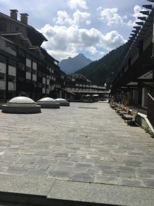 a large courtyard with benches and buildings and mountains at Condominio Colmet in La Thuile