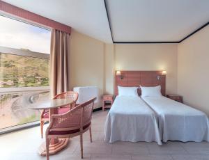 a bedroom with a bed and a table and a large window at Dom Pedro Madeira in Machico