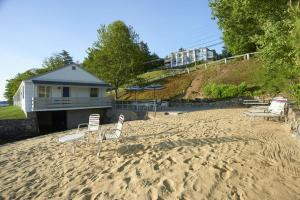 a sandy beach with two chairs and a house at Belknap Point Inn in Gilford