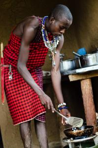 un hombre en un delantal cocinando comida en una sartén en Maji Moto Maasai Cultural Camp, en Narok