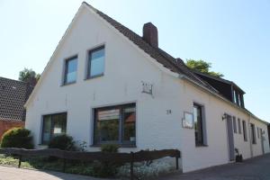 ein weißes Haus mit schwarzen Fenstern auf einer Straße in der Unterkunft Ferienwohnungen im Gästehaus Sieberns in Carolinensiel