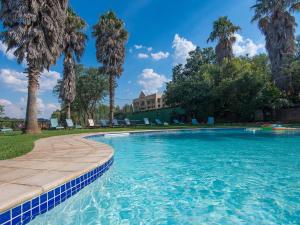 a swimming pool with palm trees and a house in the background at Glenburn Lodge & Spa in Muldersdrift