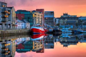 a red boat is docked in a harbor with buildings at Galway City Centre Apartment, Augustine Street in Galway
