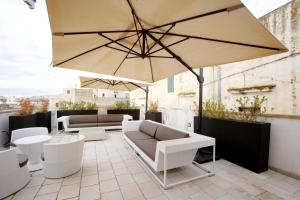 un patio con un grande ombrellone, sedie e tavoli di Vico Regio Hotel a Casarano