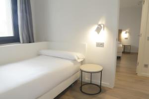 a white bed with a stool next to a window at Viviendas Oviedo Catedral in Oviedo