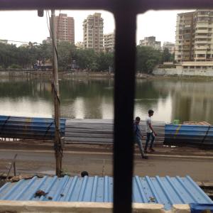 two children walking by a river with buildings in the background at Bandra Dormitory in Mumbai