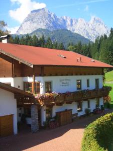 a building with a red roof with mountains in the background at Landhaus Huber in Kirchdorf in Tirol