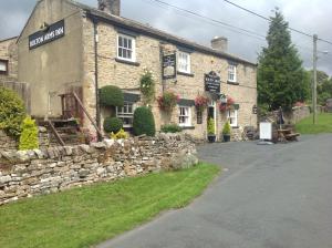 a stone building with a stone wall next to a street at Bolton arms downholme in Richmond