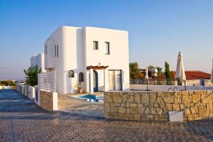 a white building with a stone wall next to a street at Meltemi Villas in Paphos City