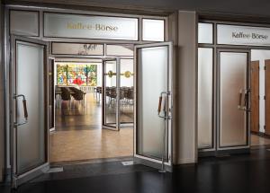 a lobby with three glass doors and a dining room at AMERON Hamburg Hotel Speicherstadt in Hamburg