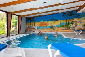 Eine Familie schwimmt in einem Schwimmbecken mit einem Wandgemälde in der Unterkunft Hotel Schoos in Fleringen