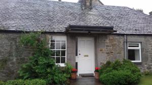a stone house with a white door and windows at Highfield Cottage in Kirknewton