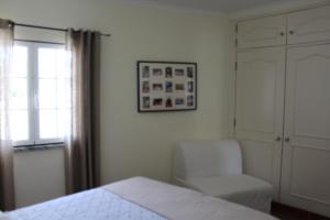 a bedroom with a bed and a chair and a window at Apartamento de São João in Praia da Areia Branca +10 photos