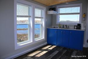 a kitchen with blue cabinets and windows with a view of the ocean at Toulinguet Inn - Suites in Twillingate