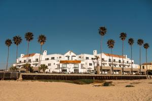 Sandcastle Hotel on the Beach في شاطئ بيسمو: مبنى أبيض كبير على الشاطئ مع أشجار النخيل