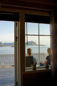 a man and woman sitting in a window looking out at the water at Nyken Resort - The apartment in Nyksund