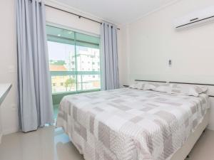 Dormitorio blanco con cama y ventana grande en Aruba en Bombinhas