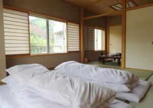 uma cama grande com lençóis brancos num quarto com janelas em Itoen Hotel Shikisai em Yugawara