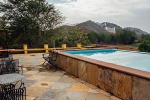 a swimming pool with chairs and tables on a patio at Devra Udaipur in Udaipur