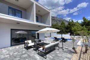 eine Terrasse mit einem Tisch, Stühlen und einem Sonnenschirm in der Unterkunft Villa Navis HEATED POOL in Makarska