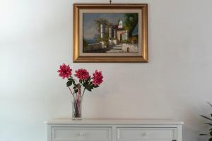 a vase with flowers on a dresser under a painting at Residenza d'epoca Olimpia in Santa Maria di Castellabate