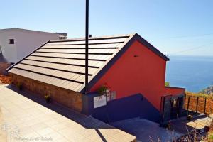 ein rotes Gebäude mit einem Dach mit dem Ozean im Hintergrund in der Unterkunft Palheirinho da Achada in Arco da Calheta