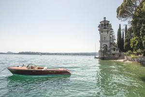 a boat in the water next to a tower at Hotel Villa Fiordaliso in Gardone Riviera