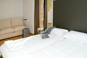 2 camas blancas en una habitación con sofá en Hospedium Hotel Convento de Santa Ana, en Atienza