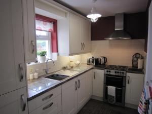 Glenarm的住宿－The Lookout, Glenarm，厨房配有白色橱柜、水槽和炉灶。