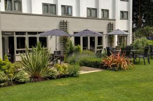 a building with tables and umbrellas in a garden at Best Western Plus Pinewood Hotel, Manchester Airport South Handforth in Handforth