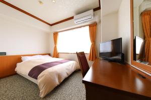 a bedroom with a bed and a desk with a television at Business Hotel Star in Beppu
