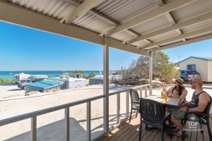zwei Personen sitzen an einem Tisch auf einer Terrasse mit Blick auf den Strand in der Unterkunft Tasman Holiday Parks - Denham Seaside in Denham