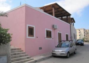 潘泰莱里亚Dammuso Lubo的一座粉红色的建筑,前面有一辆汽车
