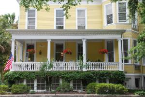 ein gelbes Haus mit einer weißen Veranda und einer amerikanischen Flagge in der Unterkunft Forsyth Park Inn in Savannah