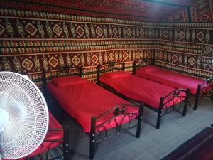 a room with three red beds and a fan at Climbers House in Wadi Rum in Wadi Rum
